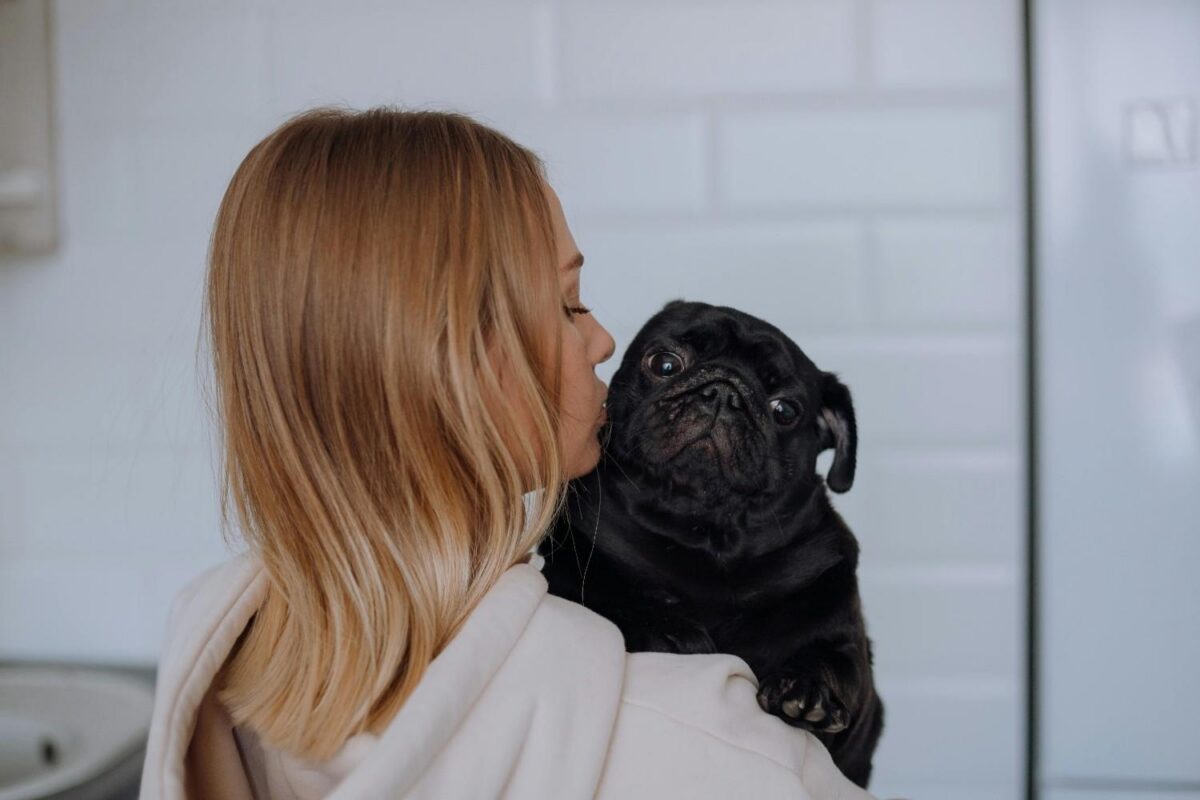 A woman embraces a black pug in an indoor setting