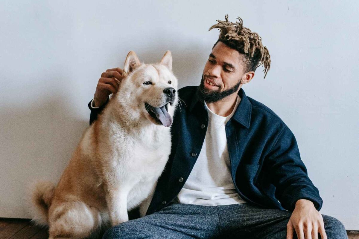 A young man with dreadlocks lovingly pats his Akita Inu dog indoors