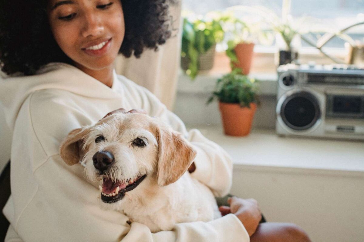 A smiling woman in a cozy hoodie embraces her happy dog indoors