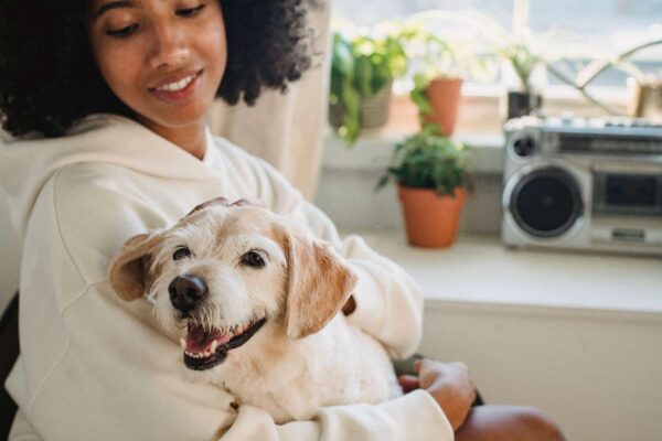 A smiling woman in a cozy hoodie embraces her happy dog indoors